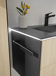 Badezimmer Riana: Detail umlaufende Fugenbeleuchtung mit Bewegungsmelder, LEDplus-fähig (Kalt-, Neutral- oder Warmlicht schaltbar und dimmbar, 18,1 Watt) unter Waschtisch Duratek-Granit (BME018F10011) schwarz matt, inkl. Armaturbohrung und integriertem Überlauf, ca. B 101, H 1, T 49 cm, Waschtischunterschrank (W01018F10) , 2 Auszüge, ca. B 99, H 48, T 48 cm, Korpus Schwarz-Matt-Touch, Front Linea-Eiche-hell-Nachbildung (PG 1), Griffleiste schwarz mattZubehör: LEDplus-Sensorschalter (ZCS008E) für Waschtischunterschrank, Waschtischarmatur (ZEHM37) schwarz matt, Handtuchhalter (ZHH00832) für Korpusmontage, schwarz matt, ca. L 33 cm