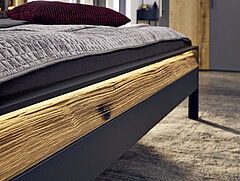 Detail ligbed-voetbord met ledverlichting in lak grafiet / afwerking massief wild eiken geborsteld met gekloofd hout