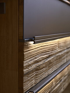 Waschtisch-Hängeschrank 810128 mit 1 Auszug oben (Colorglas graphit / Absetzung Spaltholz Altholz-Eiche, lackiert) und 1 Schubkasten unten (Spaltholz), ca. B 120,0, H 57,6, T 50,0 cm, Griffleisten Metall Lack titan mit LED-Griffbeleuchtung 810912