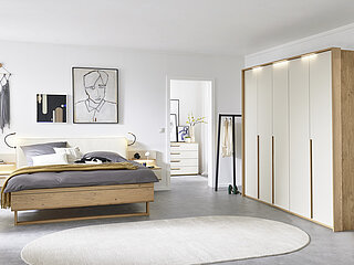 Vorschlag 701, Balkeneiche furniert, Absetzung Lack Sand, bestehend aus Drehtürenschrank 6-türig, 3 Griffstangen in Eiche massiv, ca. B 299, H 229, T 60 cm, Doppelbett in Luxushöhe, ca. B 189, H 105, T 222 cm, Liegefläche ca. 180 x 200 cm, BSH 48,6 cm, Polsterkopfteil "Luna" in Stoff Maranta Sand, 100 % Polyester, Fußteil mit Lisene, unten abgerundet und Kufe in Eiche, 2 Hängekonsolen mit je 1 Schubkasten, jeweils ca. B 60, H 23, T 46 cm. Zubehör: Passepartout ohne Beleuchtung (903004); 3er-Set LED-Stabbeleuchtung (90353); Paneelaufsatz links und rechts mit Holzboden (20216, 20226); indirekte LED-Holzbodenbeleuchtung (80027); 2er-Set LED-Flex-Leuchte Anthrazit, USB-Anschluss (80033).