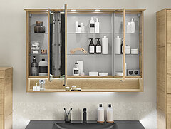 Badezimmer Riana: Detail geöffneter Spiegelschrank, einfach verspiegelt, mit Griffset schwarz matt, unten 1 offenes Fach inkl. LEDplus-Beleuchtung